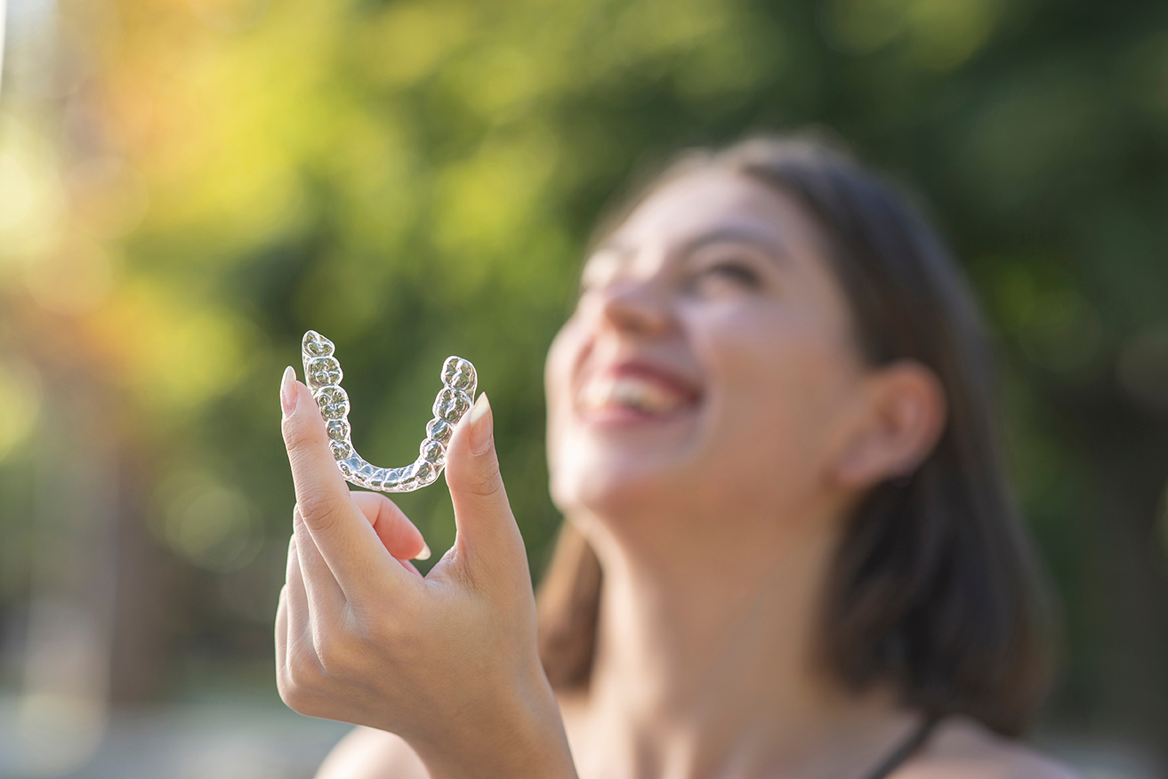 woman holding up invisalign clear dental aligners smiling